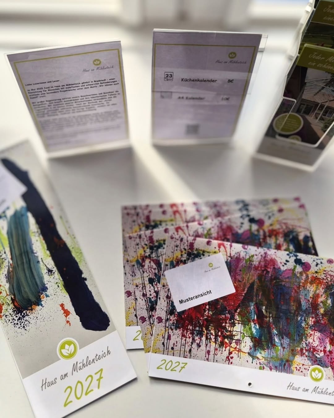Kalender mit farbenfrohen Action-Painting-Motiven aus dem Haus am Mühlenteich, ausgelegt mit Informationsaufstellern